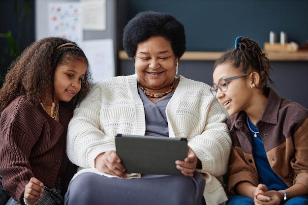 A diverse group of children in a Spanish classroom using tablets for learning, with a teacher assisting them; emphasis on inclusivity and modern technology in education.