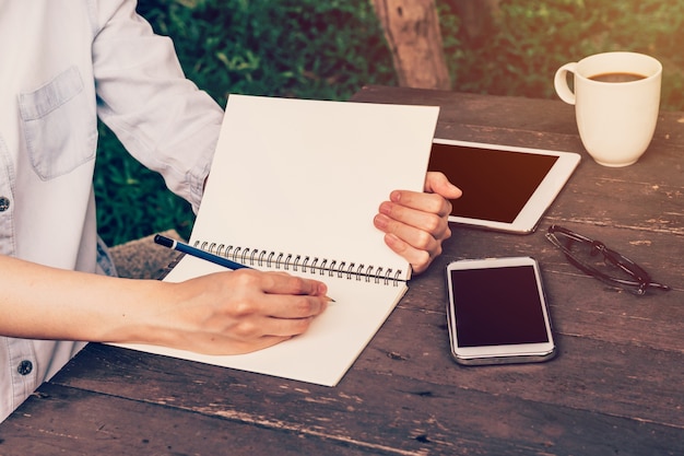 A person writing on a notebook with a pen, another person writing on a notepad in the background