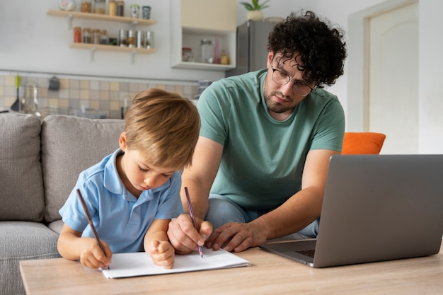 A father sitting at a table with his child, using an educational guide to help with homework, fostering a supporting and engaging learning environment at home.