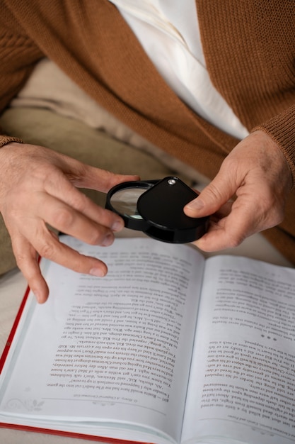 A close-up of a person's hands holding a guidebook, with a magnifying glass resting on the page. The focus is on the details of the guidebook's content and the act of careful examination.