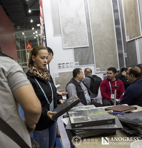 A developer showcase event in Madrid, Spain. The image features several booths where developers display their VR games and technologies. The focus is on a young developer demonstrating a VR game to a group of interested attendees wearing VR headsets. The scene is lively with many people trying out the games and networking. Banners of Spanish game development companies are visible in the background.