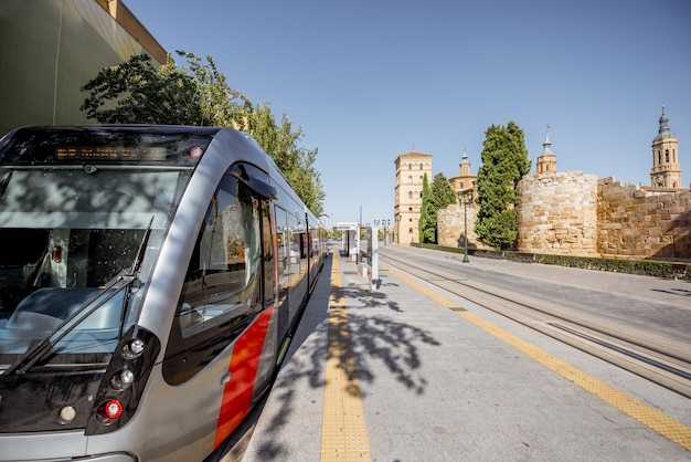 A street scene in Valencia, Spain, showing modern electric buses, bicycle lanes, and smart street lighting. The environment is clean and green, with trees lining the sidewalks and pedestrians using digital information kiosks.