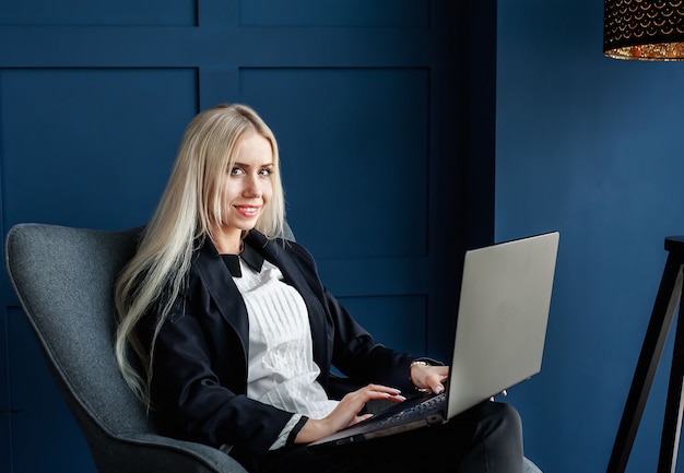 A professional woman in a business suit, smiling confidently while using a laptop in a modern co-working space. The background includes blurred images of other professionals collaborating, highlighting a dynamic and supportive work environment. The focus is on her empowerment and career progression.