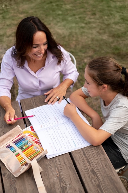 A parent is filling out an application form at a desk, with a child sitting beside them, looking at colorful books. The scene suggests the process of applying for childcare assistance.
