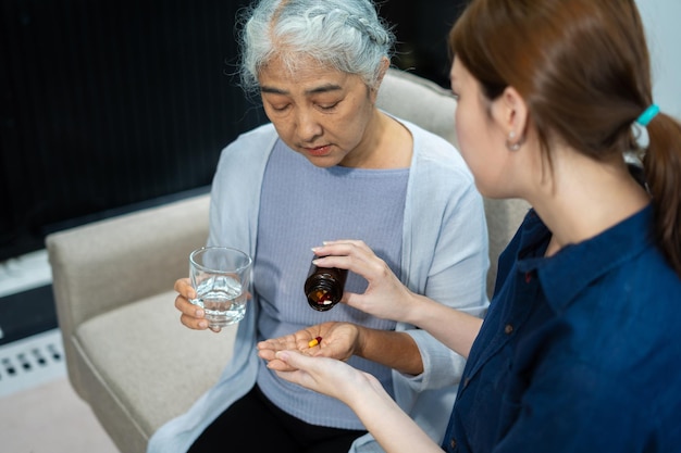 A caregiver assisting an elderly woman with her medication. They are sitting at a table with pill organizers and water. The scene signifies careful attention and support in managing health needs.