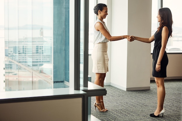Close-up of two business people in a modern office in Singapore, shaking hands and smiling, with the Singapore skyline visible through the window in the background. Capture their determined cooperation in the scene.